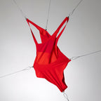 Maillot de bain une pièce rouge haut de gamme, mis sous tension par des câbles pour souligner sa technicité.